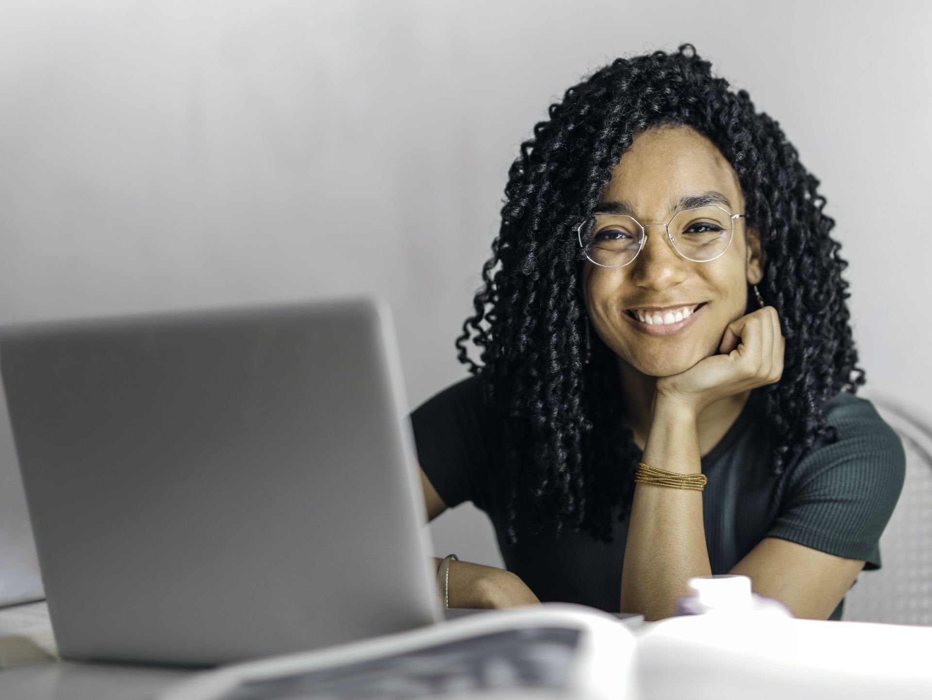 Happy ethnic woman sitting at table with laptop